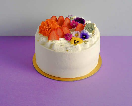 Cake decorated with fresh strawberries and edible flowers, coated with Madagascan vanilla bean cream. 