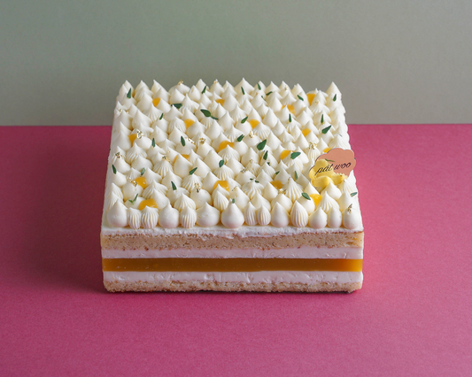 A layered mousse cake topped with whipped cream, mango jelly and gold foil decorations. Features layers of light sponge cake infused with Koichi yuzu.